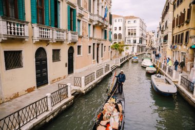 İtalya düğünü Venedik 'te. Gondolcu bir gelin ve damadı dar bir Venedik kanalı boyunca klasik bir ahşap gondola sarar. Yeni evliler antik binaların arka planında bir teknede oturuyorlar..