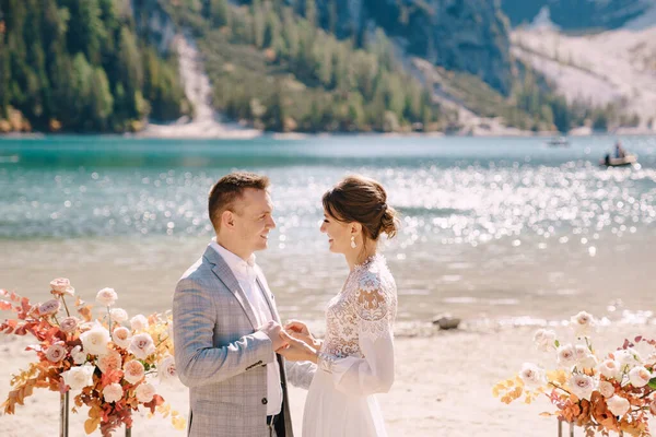Vor der Kulisse des Pragser Sees in Italien stehen Braut und Bräutigam mit einem Bogen herbstlicher Blumensäulen an Ort und Stelle für die Zeremonie. Destination Hochzeit in Europa, am Pragser See. — Stockfoto