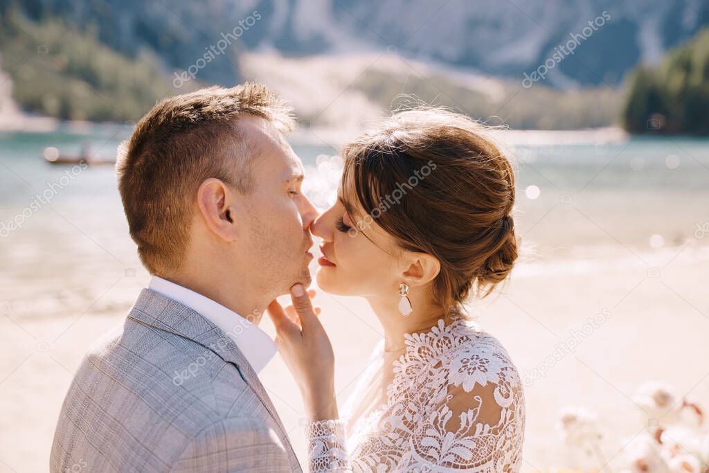 The newlyweds kiss on the spot for the ceremony, with an arch of autumn flower columns, against the backdrop of the Lago di Braies in Italy. Destination wedding in Europe, on Braies lake.