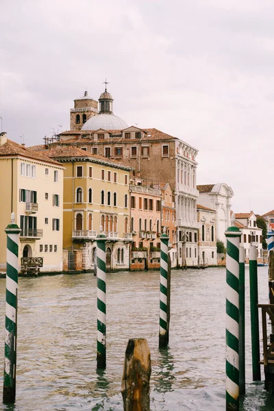 Vista de los edificios en el Gran Canal, Venecia, Italia, a través de postes de rayas verdes - un muelle para góndolas y barcos . — Foto de Stock