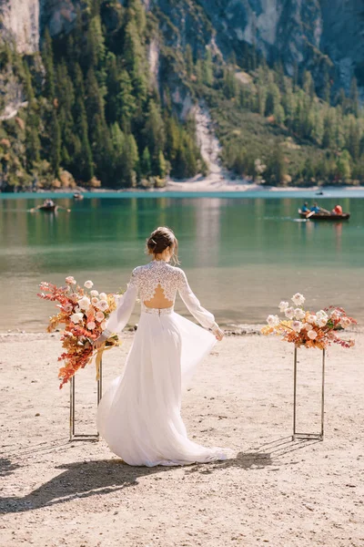 Bela noiva em um vestido branco com mangas e rendas, com um buquê de outono amarelo no fundo do arco para cerimônia, no Lago di Braies, na Itália. Casamento de destino na Europa, no lago Braies . — Fotografia de Stock