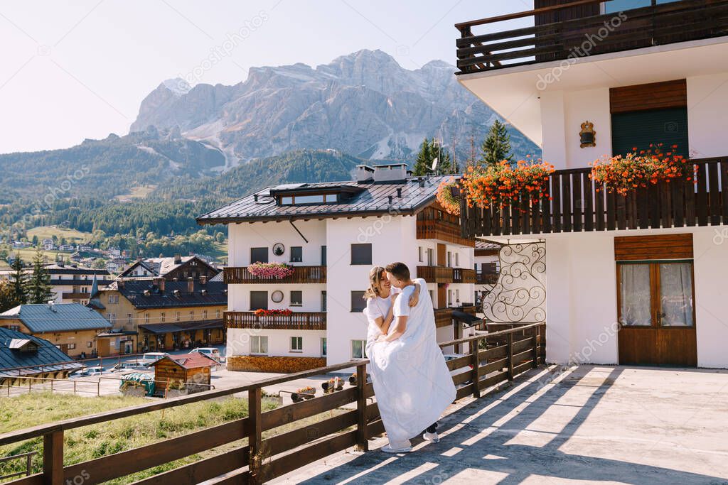 A guy and a girl cuddle with a blanket outside a hotel in the mountains. Cortina Ampezzo is an Italian city in province of Belluno in Veneto region, a winter resort in Dolomites