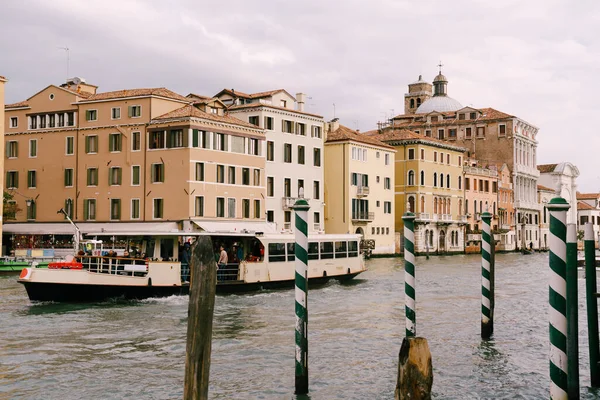 Vaporetto: tranvía fluvial, barco de enlace, transporte principal en la parte insular de Venecia. Turistas en el paseo marítimo en Venecia, sobre el fondo de las antiguas fachadas de los edificios de pie en el agua — Foto de Stock