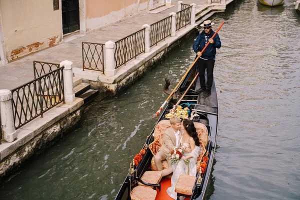 Венеція, Італія - 04 жовтня 2019: Італійське весілля у Венеції. Гондольєр кидає наречену з нареченим у класичну дерев'яну гондолу по вузькому венеціанському каналу. Молоді сидять у човні. — стокове фото