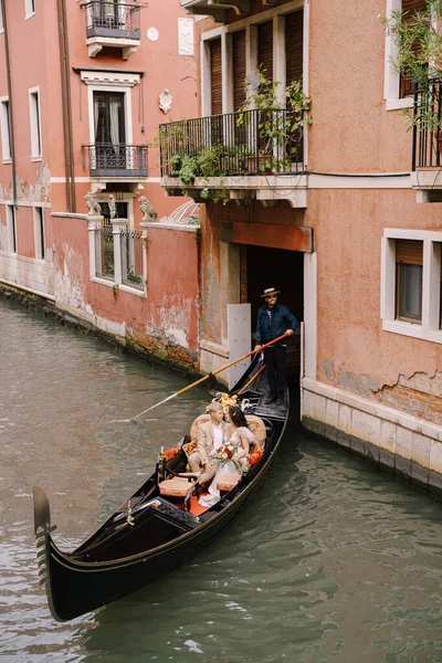 Венеція, Італія - 04 жовтня 2019: Італійське весілля у Венеції. Гондольєр кидає наречену з нареченим у класичну дерев'яну гондолу по вузькому венеціанському каналу. Човен виходить з рожевого будинку. — стокове фото