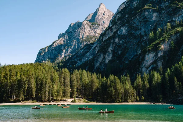 Tourists swim in wooden boats on the Lago di Braies amid rocky mountains and forests. Braies lake in the Dolomites in South Tyrol, Italy, a municipality of Braies, in the Prague Valley.