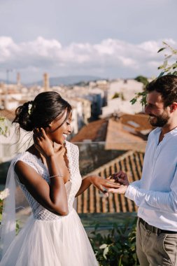 Çok ırklı bir çift, Afro-Amerikalı gelin ve beyaz damat. Damat gelinin parmağına yüzük takar. İtalya, Floransa 'da güzel sanatlar yapılan bir düğün. Çatıda düğün seremonisi