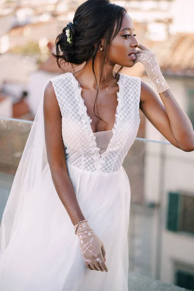 Beautiful African American bride in a white wedding dress, touches her face in vintage gloves. Fine-Art Wedding in Florence, Italy.