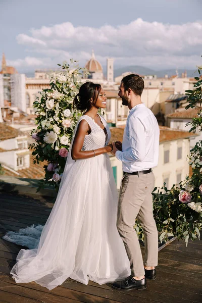 Pasangan pernikahan antar ras. Sebuah upacara pernikahan di atap bangunan, dengan pemandangan kota dan Katedral Santa Maria Del Fiore. Tujuan pernikahan seni rupa di Florence, Italia — Stok Foto