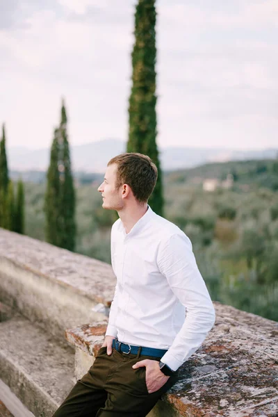Великий чоловічий портрет на даху старої виноробної вілли в Тоскані, Італія. Біла сорочка з довгими рукавами, розумні годинники, синій пояс, руки в кишені штанів. — стокове фото