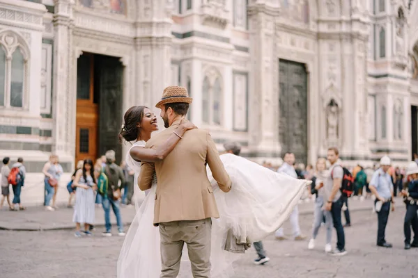 Pasangan pernikahan antar ras. Pernikahan di Florence, Italia. Pengantin pria kulit putih lingkaran dan ciuman pengantin Afrika-Amerika di Piazza del Duomo. Stok Foto Bebas Royalti