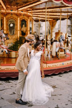 Interracial wedding couple. Wedding in Florence, Italy. African-American bride and Caucasian groom near the carousel. clipart