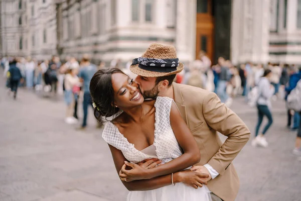 Pasangan kawin campuran-ras. Pernikahan di Florence, Italia. Pengantin pria kulit putih berpelukan dari belakang dan mencium pengantin wanita Afrika-Amerika. — Stok Foto
