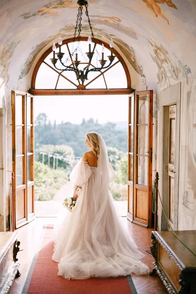 Svatba ve staré vinařské vile v Toskánsku v Itálii. Nevěsta se prochází v interiéru vily, s výhledem do zahrady. — Stock fotografie