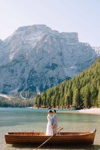 Νύφη και γαμπρός σε μια ξύλινη βάρκα στο Lago di Braies στην Ιταλία. Γαμήλιο ζευγάρι στην Ευρώπη, στη λίμνη Μπρέις, στους Δολομίτες. Οι νεόνυμφοι στέκονται στη βάρκα και αγκαλιάζονται. — Φωτογραφία Αρχείου