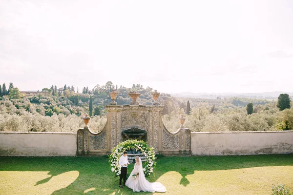 Весілля на старому виноробному віллі в Тоскані, Італія. Весільна пара під круглою аркою квітів. Наречений читає шлюбні обітниці.. — стокове фото
