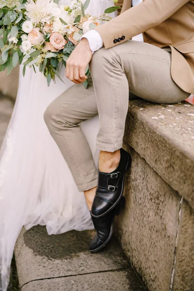 Pernikahan di Florence, Italia. Close-up dari kaki pengantin pria dengan celana pendek ringan dan sepatu kulit hitam, pengantin wanita dengan gaun putih dengan buket di tangannya. Stok Foto