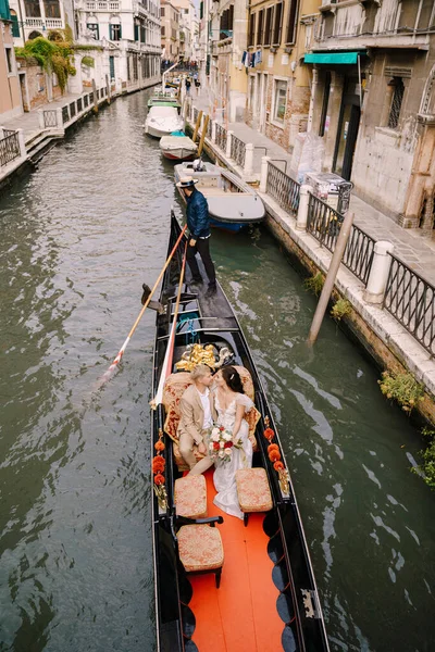 Venecia, Italia - 04 de octubre de 2019: Italia boda en Venecia. Un gondolero enrolla a los novios en una clásica góndola de madera a lo largo de un estrecho canal veneciano. Los recién casados están sentados en un barco — Foto de Stock