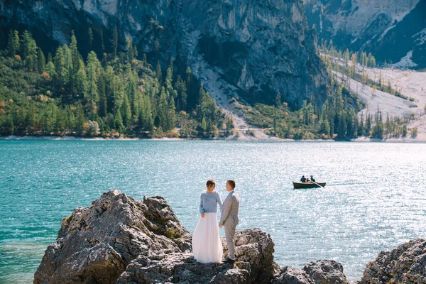 Das Brautpaar steht auf Steinen mit Blick auf den Pragser See in Italien. Destination Hochzeit in Europa, am Pragser See. Liebevolles Brautpaar spaziert vor der Kulisse der atemberaubenden Natur. — Stockfoto