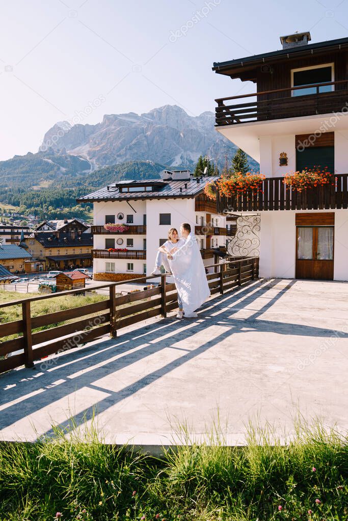A guy and a girl cuddle with a blanket outside a hotel in the mountains. Cortina Ampezzo is an Italian city in province of Belluno in Veneto region, a winter resort in Dolomites