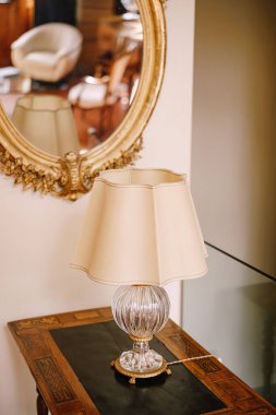 Beyaz abajur ve kristal tabanlı antika masa lambası. Altın çerçeveli antik ayna.