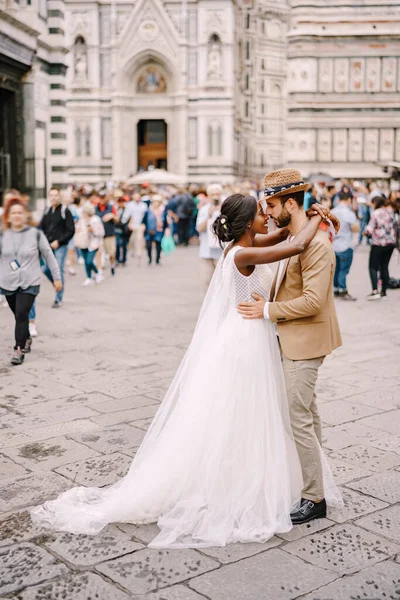 Fajok közötti házaspár. Esküvő Firenzében, Olaszországban. Afrikai-amerikai menyasszony és kaukázusi vőlegény ölelés Piazza del Duomo-ban. — Stock Fotó