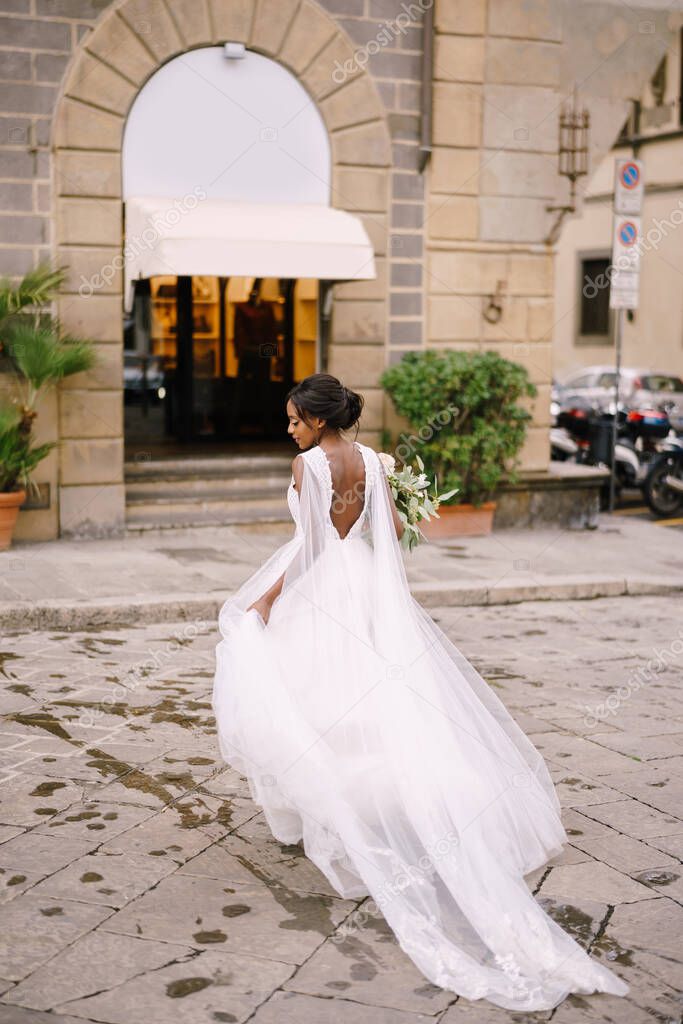 Wedding in Florence, Italy. African-American bride in a white dress with a long veil and a bouquet in her hands.