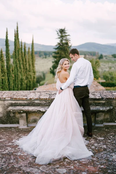 Pernikahan di sebuah vila anggur tua di Tuscany, Italia. Pasangan yang menikah berdiri di atap sebuah anggur tua, berpelukan, berdiri dengan punggung ke bingkai. — Stok Foto