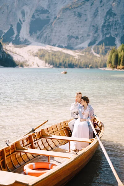 Een bruidspaar zit in een houten boot op het Lago di Braies in Italië. Pasgetrouwden in Europa, op Braies Lake, in de Dolomieten. De bruidegom knuffelt de bruid. — Stockfoto