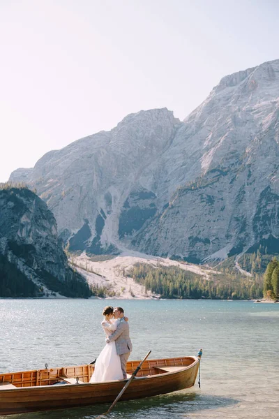 Mariée et marié naviguant en bateau en bois, avec des rames au lac Lago di Braies en Italie. Mariage en Europe - Les jeunes mariés se tiennent debout dans un bateau . — Photo