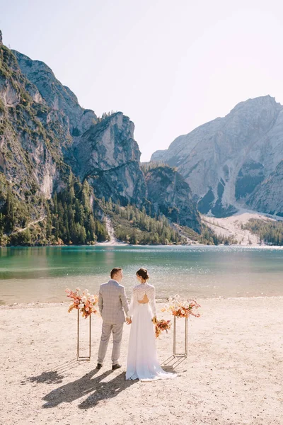 Les mariés se tiennent en place pour la cérémonie, avec un arc de colonnes de fleurs d'automne, dans le contexte du lac des Braies en Italie. Mariage de destination en Europe, sur le lac de Braies . — Photo