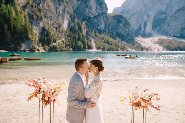 Жених надевает кольцо на невесту, на месте церемонии, с аркой осенних цветочных колонн, на фоне Лаго ди Брайс в Италии. Свадьба в Европе, на озере Брайс — стоковое фото