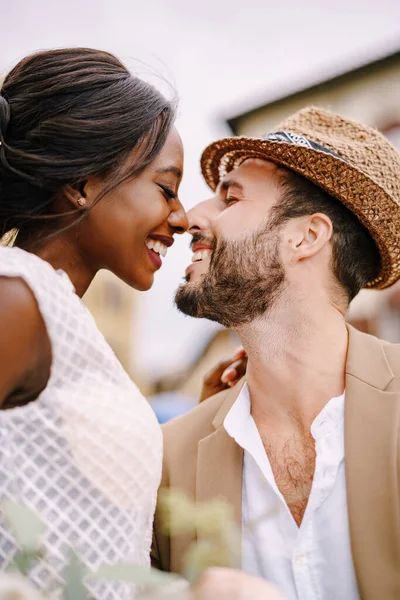 Pasangan pernikahan antar ras. Pernikahan di Florence, Italia. Foto close-up dari seorang pengantin Afrika-Amerika dan pengantin pria Kaukasia dengan topi jerami. Stok Gambar