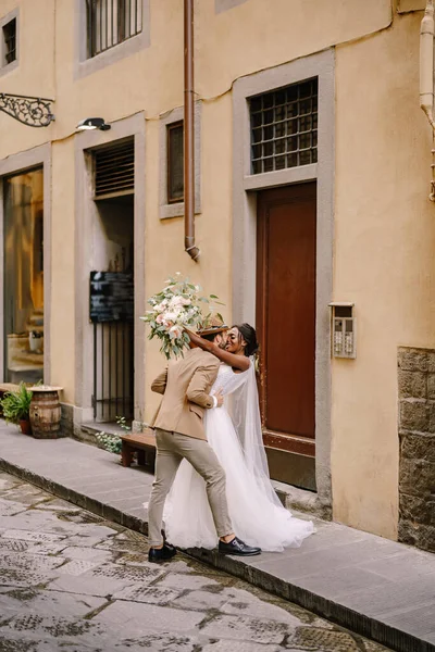 Fajok közötti házaspár. Esküvő Firenzében, Olaszországban. Afrikai-amerikai menyasszony és fehér vőlegény csók az utcán. — Stock Fotó