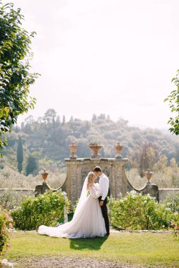 Gelin ve damat parkta yürürler. Tuscany, İtalya 'da eski bir şaraphane villasında düğün. Yuvarlak düğün kemeri beyaz çiçekler ve yeşillikle süslenmiş eski bir İtalyan mimarisinin önünde..