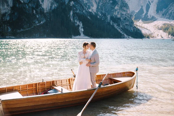 Menyasszony és vőlegény vitorlázás fa hajó, evezők Lago di Braies tó Olaszországban. Esküvő Európában - A friss házasok egy csónakban ölelkeznek. — Stock Fotó