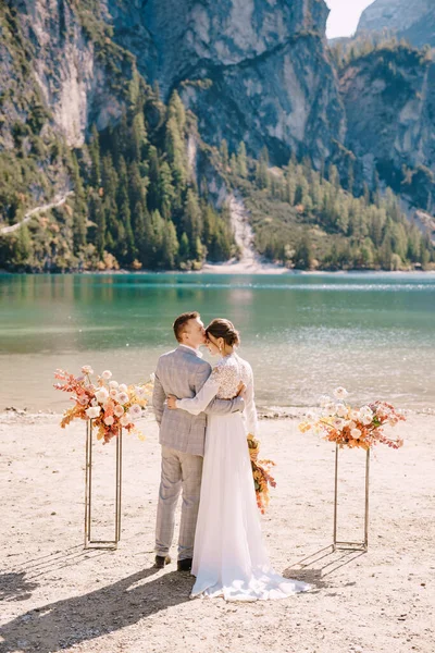 Les mariés se tiennent en place pour la cérémonie, avec un arc de colonnes de fleurs d'automne, dans le contexte du lac des Braies en Italie. Mariage de destination en Europe, sur le lac de Braies . — Photo