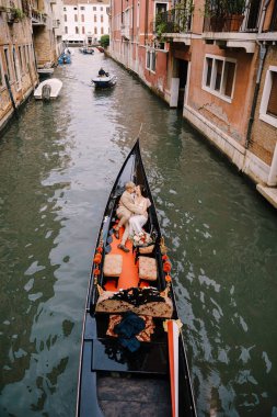 İtalya düğünü Venedik 'te. Gondolcu bir gelin ve damadı dar bir Venedik kanalı boyunca klasik bir ahşap gondola sarar. Yeni evliler antik binaların arka planında bir teknede oturuyorlar..