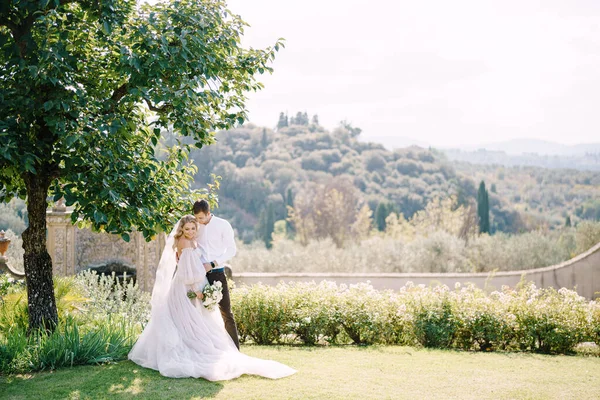 Pernikahan di Florence, Italia, di sebuah villa-winery tua. Mempelai pria dan wanita di bawah pohon. Pasangan pernikahan berjalan di taman. — Stok Foto