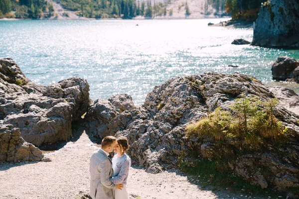 Bruid en bruidegom staan tegen de achtergrond van stenen met uitzicht op Lago di Braies in Italië. Bestemmingsbruiloft in Europa, aan het Braies meer. Liefdevolle pasgetrouwden wandelen tegen de achtergrond van de verbazingwekkende natuur. — Stockfoto