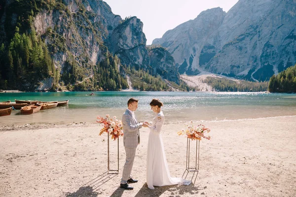 결혼식을 위해 신부는 이탈리아 의라고 디 브라이 어스를 배경으로 가을 꽃 기둥의 아치와 함께 신랑에게 반지를 걸고 있다. 유럽의 브레 이브스 호수에서의 목적지 결혼식. — 스톡 사진