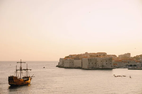 La ciudad vieja de Dubrovnik contra el cielo del atardecer. El velero de madera Galeón se acerca al muelle principal de Dubrovnik . — Foto de Stock