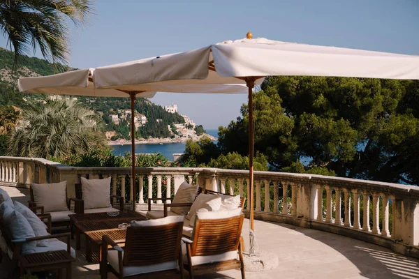 Terület Villa Sheherezade. Dubrovnik legjobb szállodái. Kerti fa bútorok fehér párnákkal, egy nagy napernyő alatt. Kerítés kőoszlopokkal, kilátás az Adriai-tengerre. — Stock Fotó