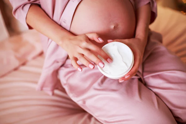 Mi sto prendendo cura. Donna incinta spargere crema sulla pancia nella sua camera da letto . — Foto Stock