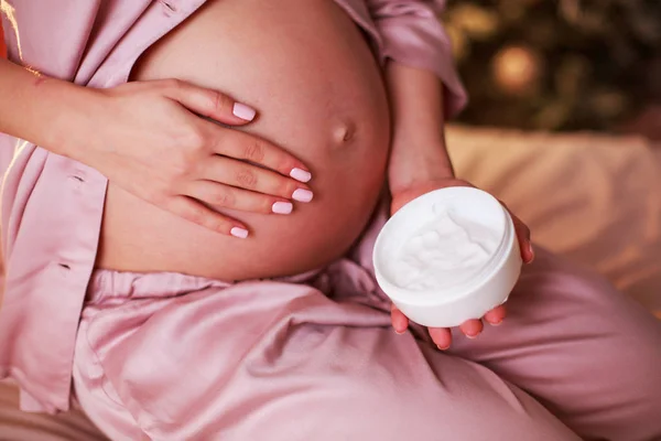Ik zorg goed. Zwangere vrouw verspreiden crème op haar buik in haar slaapkamer. — Stockfoto