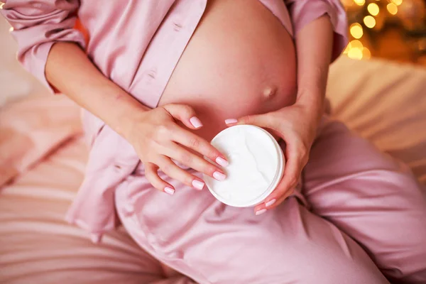 Ik zorg goed. Zwangere vrouw verspreiden crème op haar buik in haar slaapkamer. — Stockfoto