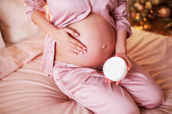 Estou a tomar cuidado. Mulher grávida espalhando creme em sua barriga em seu quarto . — Fotografia de Stock