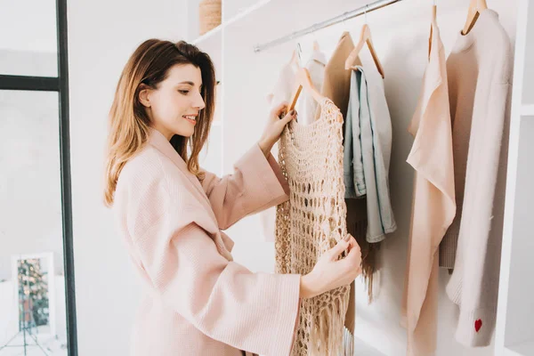 Leuke jonge vrouw staan in de voorkant van hanger rack en proberen om outfit te kiezen. — Stockfoto