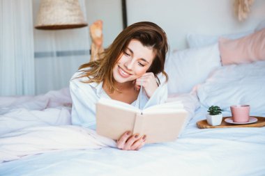 Kitap okuyan, kahve ya da çay içen, yatakta dinlenen bir kız..