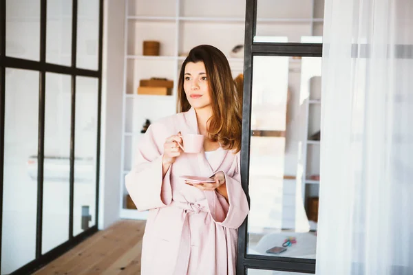 Mooi meisje in een badjas genieten van koffie thuis. — Stockfoto